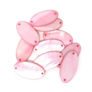 Puede incluir: Un grupo de cuentas ovaladas de concha rosa con dos agujeros cada una. Las cuentas son lisas y tienen un brillo nacarado.