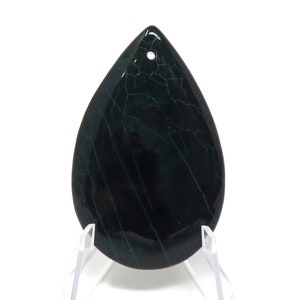 Puede incluir: Un colgante de ágata verde oscuro con forma de lágrima y un agujero blanco en la parte superior para encordar. La ágata tiene un patrón natural de mármol con vetas blancas y verdes.