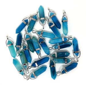 May include: A collection of blue and teal crystal pendants with silver-colored metal accents. The pendants are various shades of blue, from light teal to deep indigo, and are arranged on a white background.