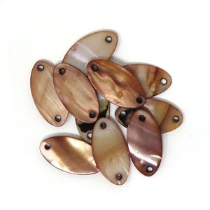 May include: A group of oval-shaped shell beads with a brown and cream color. The beads have two holes each and are perfect for jewelry making.
