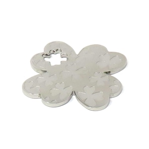 Peut inclure: Un charm en forme de trèfle à quatre feuilles de couleur argentée, orné d'un motif de trèfles. Le charm comporte un petit motif en forme de croix ouvert au centre. Le trèfle est un symbole de chance et de fortune.