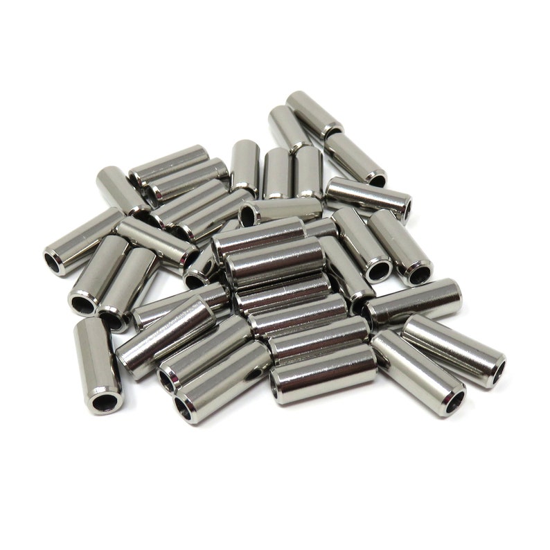 May include: A collection of shiny, silver-colored metal spacers. These cylindrical components have a hollow center and are arranged on a white background. The spacers are likely used in various mechanical or construction applications.