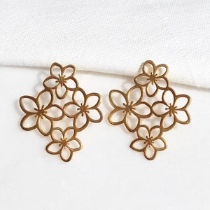 Może przedstawiać: Para złotych kolczyków z delikatnym wzorem kwiatowym. Każdy kolczyk ma pięć małych, ażurowych kwiatów ułożonych w gronie.