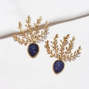 Peut inclure: Une paire de boucles d'oreilles en or avec une pierre précieuse bleue et un motif feuillu délicat.