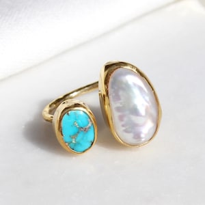 May include: Gold ring featuring a turquoise and a white pearl stone. The ring is open and can be adjusted to fit different finger sizes.