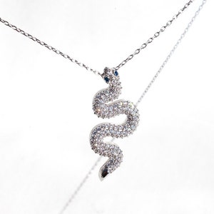 Könnte beinhalten: Eine silberne Schlangen-Anhänger-Kette mit klaren Zirkonia-Steinen und blauen Akzenten. Die Schlange ist gewickelt und hat ein detailliertes Design.