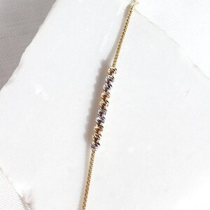 Puede incluir: Una delicada pulsera de cadena dorada con una serie de cuentas esf&eacute;ricas texturizadas en oro, plata y oro rosa. La pulsera se muestra sobre una superficie blanca, mostrando su intrincado dise&ntilde;o y variaciones de color. Esta joya es adecuada para el uso diario.