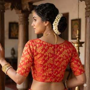Könnte beinhalten: Eine rote Bluse mit goldenen Blumenmustern und kurzen Ärmeln. Die Bluse hat einen runden Ausschnitt und eine Reihe von Knöpfen auf der Rückseite. Die Bluse ist Teil eines traditionellen indischen Outfits.