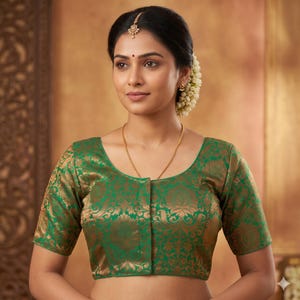 May include: A green and gold brocade blouse with short sleeves. The blouse has a scoop neckline and a floral pattern. The woman is wearing a gold necklace and earrings. She has a traditional hair style with flowers.