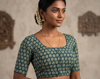 Puede incluir: Una blusa color verde azulado con cuello cuadrado y mangas cortas. La blusa presenta un patrón repetitivo de formas florales amarillo-verdosas. La mujer lleva joyas de oro, incluyendo un collar, pendientes y pulseras.