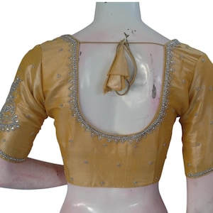 Puede incluir: Una blusa bordada de color dorado con espalda baja y mangas cortas. La blusa está decorada con lentejuelas y cuentas plateadas.