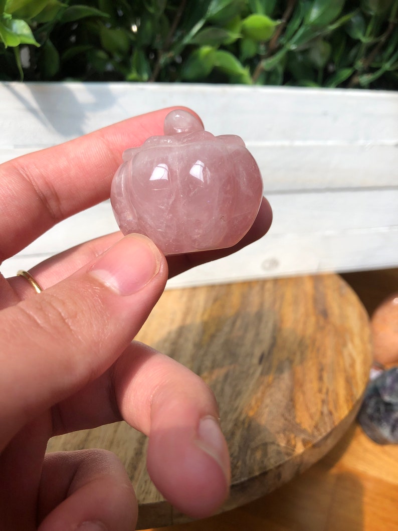 May include: A small, pink, carved rose quartz box with a lid. The box is in the shape of a pumpkin.