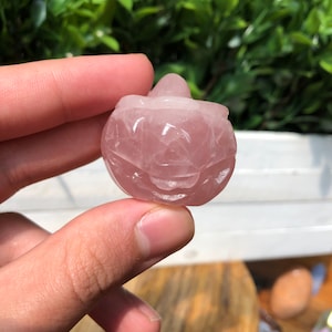 May include: A carved pink rose quartz pumpkin. The pumpkin is approximately 5 cm tall and has a smooth, polished surface.