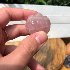 May include: A carved rose quartz sphere with a pink hue. The sphere is smooth and polished, with a delicate, intricate design.