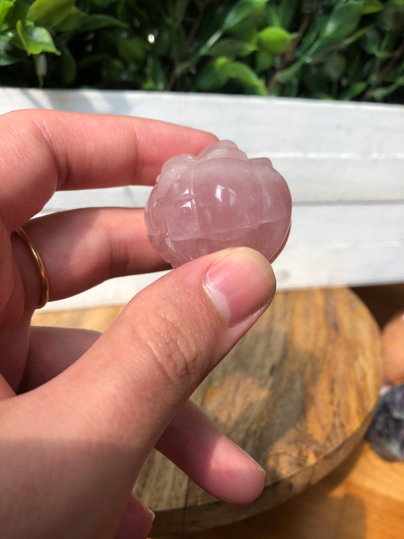 May include: A carved rose quartz sphere with a pink hue. The sphere is smooth and polished, with a delicate, intricate design.