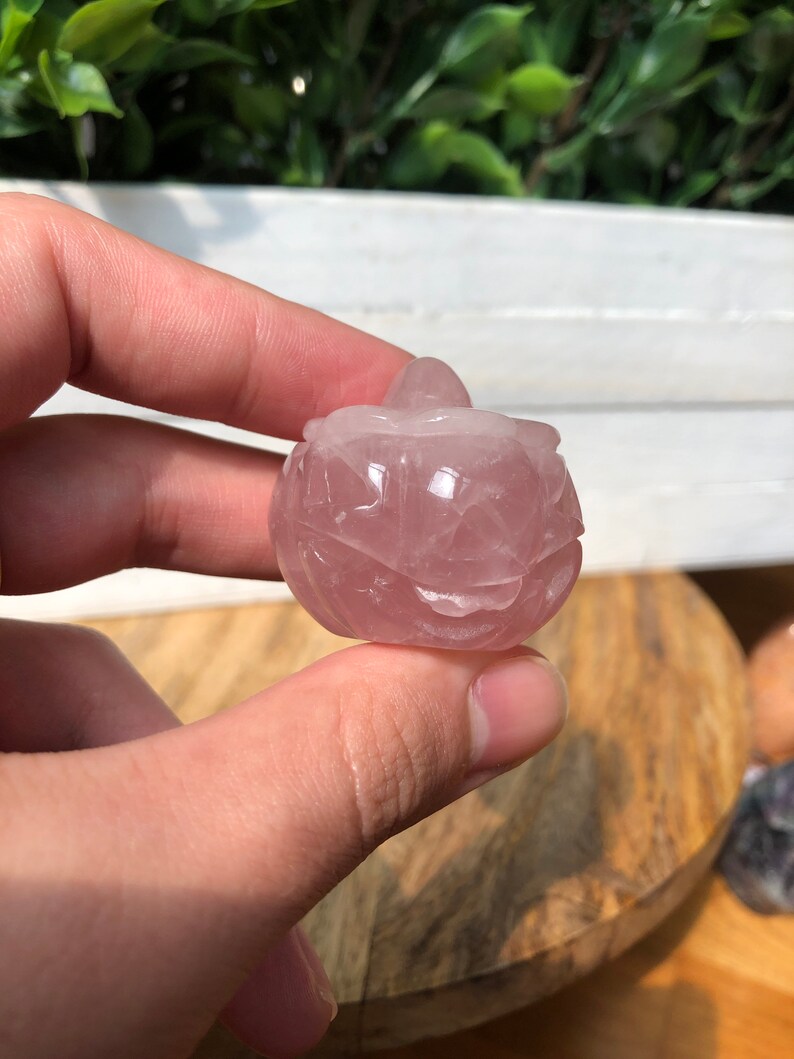 May include: A carved rose quartz pumpkin with a pink hue. The pumpkin is smooth and polished.