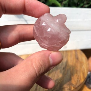 May include: A small, pink, heart-shaped rose quartz crystal. The crystal is smooth and polished, with a slightly cloudy appearance.