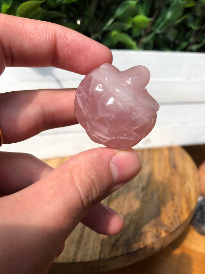 May include: A small, pink, heart-shaped rose quartz crystal. The crystal is smooth and polished, with a slightly cloudy appearance.
