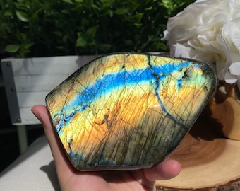 May include: A large, iridescent labradorite crystal with a blue, yellow, and black colour pattern. The crystal is smooth and polished, and it has a unique, natural shape.