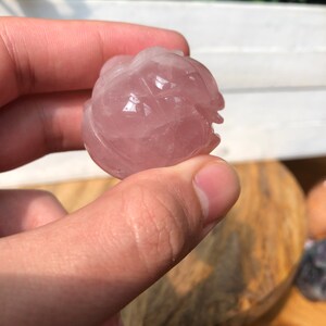 May include: A carved rose quartz sphere with a pink hue. The sphere is smooth and polished, with intricate details carved into the surface.