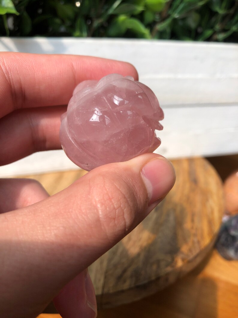 May include: A carved rose quartz sphere with a pink hue. The sphere is smooth and polished, with intricate details carved into the surface.