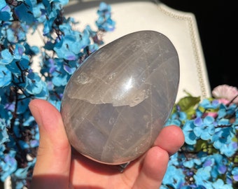 Puede incluir: Un cristal liso, gris, en forma de huevo con un patrón estriado. El cristal se sostiene en una mano.