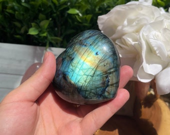 May include: A heart-shaped labradorite crystal with iridescent blue, green, and gold hues. The crystal is smooth and polished, with a natural, irregular shape.