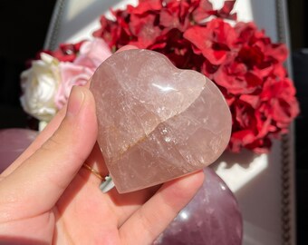 May include: A heart-shaped rose quartz crystal with a light pink hue and a translucent appearance. The crystal is smooth and polished, with a slight crack running through it.