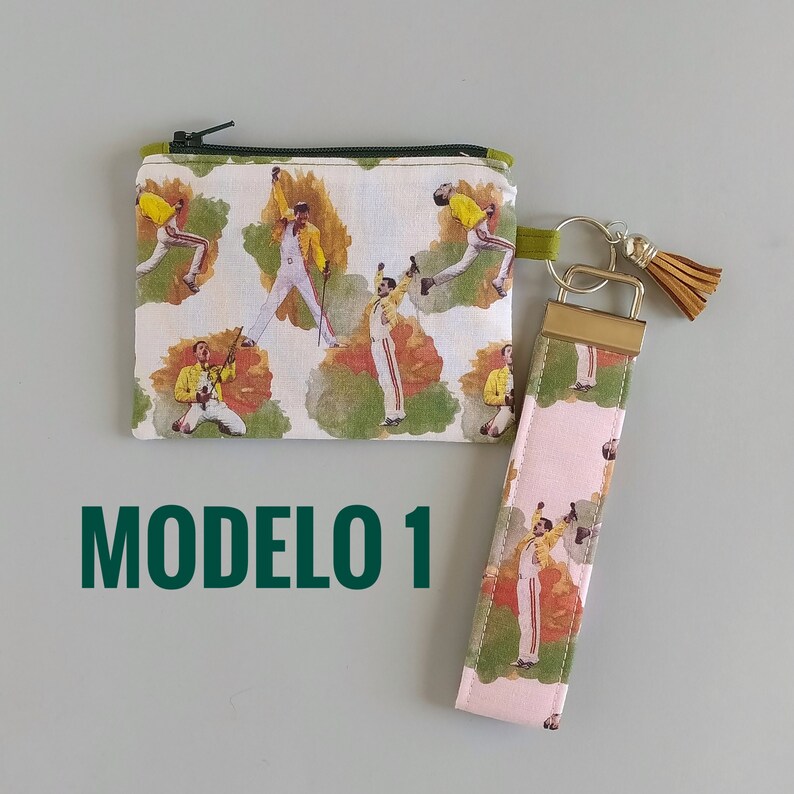 May include: A small zippered pouch and a wristlet key fob featuring a repeating pattern of a performer in a yellow jacket and white pants. The pouch has a green zipper and the wristlet has a gold-colored clasp and a brown tassel.