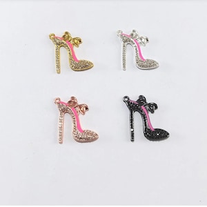 May include: Four high-heeled shoe charms in gold, silver, rose gold, and black. Each charm features a bow and is embellished with rhinestones. The heels have pink accents.