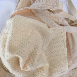 May include: A beige bra with adjustable straps and a textured, breathable cup design. The bra features a delicate lace trim along the edges and a soft, neutral colour, suitable for everyday wear. The image highlights the bra's construction and materials.