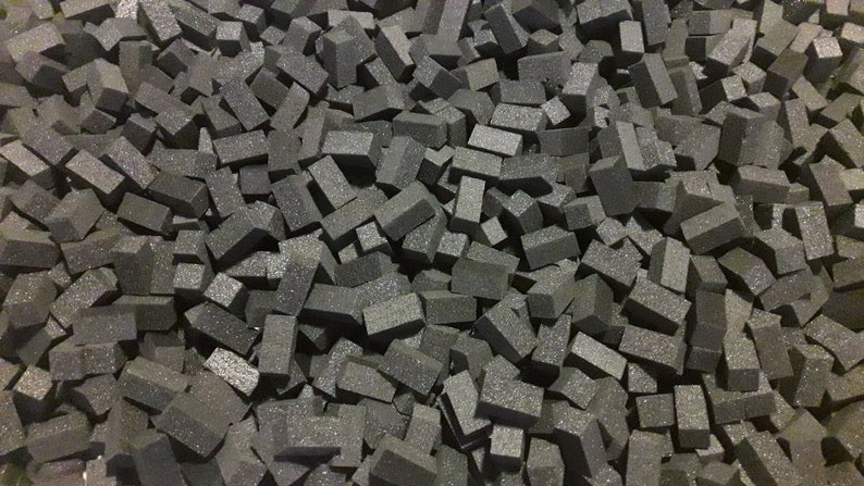 May include: A large pile of small, dark gray foam blocks. The blocks are all roughly the same size and shape, and they are arranged in a random pattern.