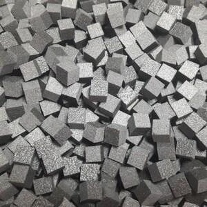 May include: A close-up image of a pile of small, gray, textured, foam cubes.