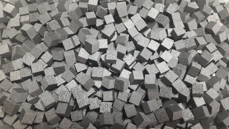 May include: A close-up image of a pile of small, gray, textured, foam cubes.