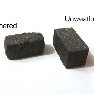 May include: Two rectangular blocks of black stone, one weathered and one unweathered. The weathered block has a rough, uneven surface, while the unweathered block has a smooth, even surface.