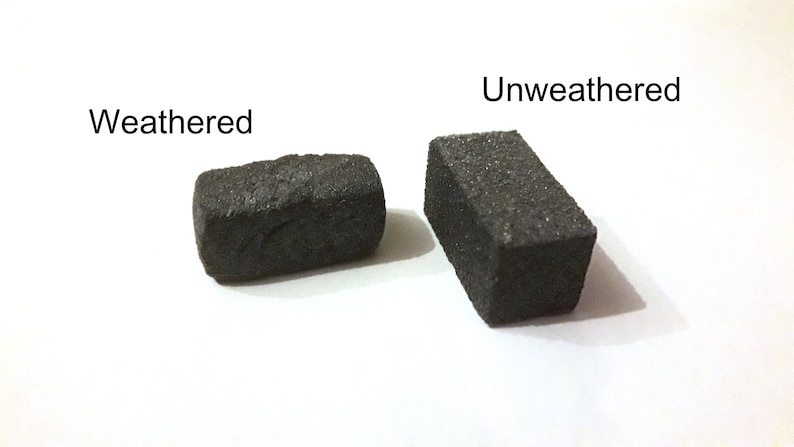 May include: Two rectangular blocks of black stone, one weathered and one unweathered. The weathered block has a rough, uneven surface, while the unweathered block has a smooth, even surface.