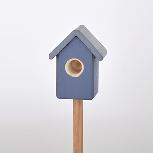Könnte beinhalten: Ein kleines blaues Vogelhaus mit einem runden Eingangsloch, montiert auf einer Holzstange.