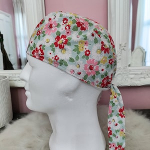 May include: A light blue and white floral print surgical cap with a red, pink, and yellow flower pattern. The cap has a tie at the back.