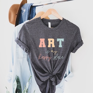 May include: A dark gray t-shirt with the text "ART is my happy place" in colorful letters. The letters are in shades of pink, yellow, blue, and green.