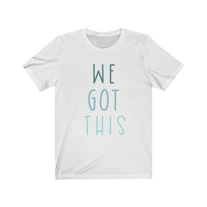Puede incluir: Camiseta blanca con el texto "WE GOT THIS" impreso en un degradado azul y verde.