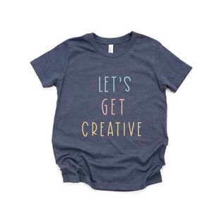 Puede incluir: Una camiseta azul marino con el texto "Let's Get Creative" en colores pastel.