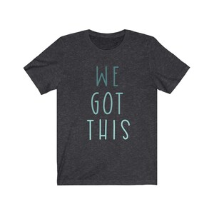 Puede incluir: Camiseta gris oscuro jaspeada con el texto "WE GOT THIS" en azul claro.
