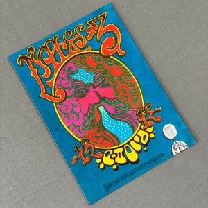 May include: A vintage poster with a psychedelic design. The poster features the word "Kisses" in large, stylized letters, and a colorful illustration of two faces kissing. The background is a vibrant blue.