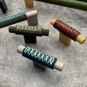 以下が含まれることがあります： 緑、青、茶色、紫など、さまざまな色の装飾的なステッチが施された革巻きキャビネットプルのおまかせセット。プルは金属ベースで、キッチン、バスルーム、または家の他のエリアで使用するために設計されています。