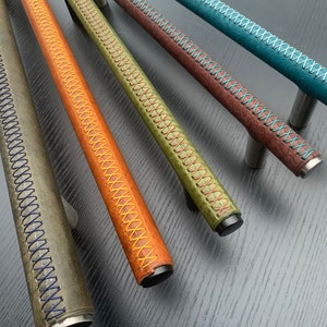 Puede incluir: Cinco tiradores de cajón de cuero en diferentes colores con costuras contrastantes. Los tiradores son todos del mismo tamaño y forma, y tienen una base de metal.