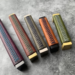 Könnte beinhalten: Fünf Leder-Schubladengriffe mit verschiedenen Farben der Nähte. Die Griffe sind alle gleich groß und in der gleichen Form, aber mit verschiedenen Farben der Nähte. Die Nähte sind ein dekoratives Detail und nicht funktional. Die Griffe sind aus Leder und haben eine Metallbasis.