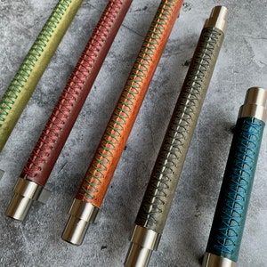 May include: Five leather drawer pulls with different colored stitching. The pulls are made of metal and have a brushed nickel finish. The stitching is in shades of green, red, blue, and brown.