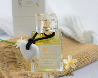 May include: A clear glass bottle of Love Organic fragrance with a black ribbon and a white heart charm. The bottle is labeled with the text "LOVE organic fragrance" and "Jasmine & Sandalwood Eau De Parfum 30ml".
