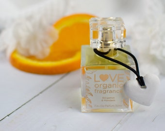 May include: A clear glass bottle of LOVE organic fragrance with a black cord and a white heart charm. The bottle is labeled with "LOVE organic fragrance Bergamot & Mandarin Eau De Parfum 30ml".