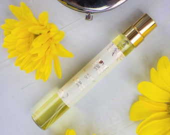 May include: A small glass bottle of Love & Fragrance orange essential oil with a gold cap and a white label with the text "Love & Fragrance, 100% pure, Orange Essential Oil, 10 ml". The bottle is surrounded by yellow flowers.